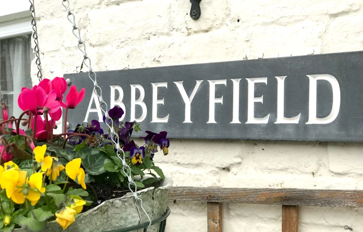 Abbeyfield sign outside the home with a hanging basket in full bloom