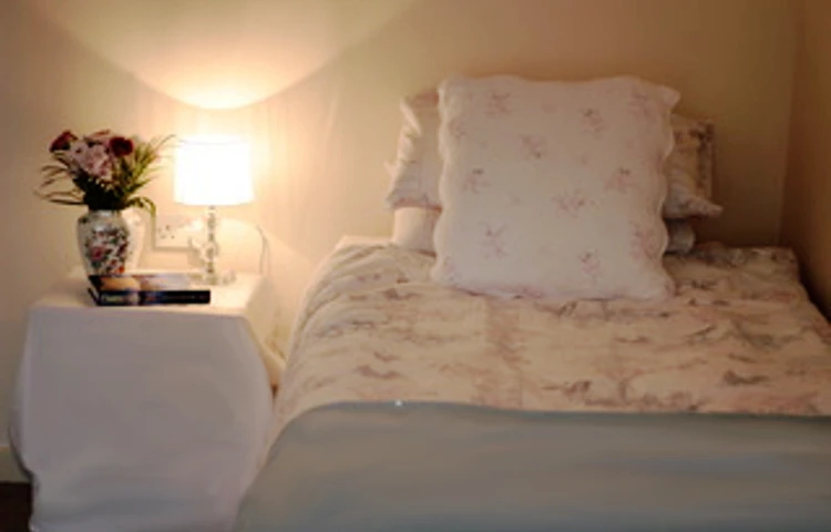 A bedroom with a lamp and flowers on the bedside table