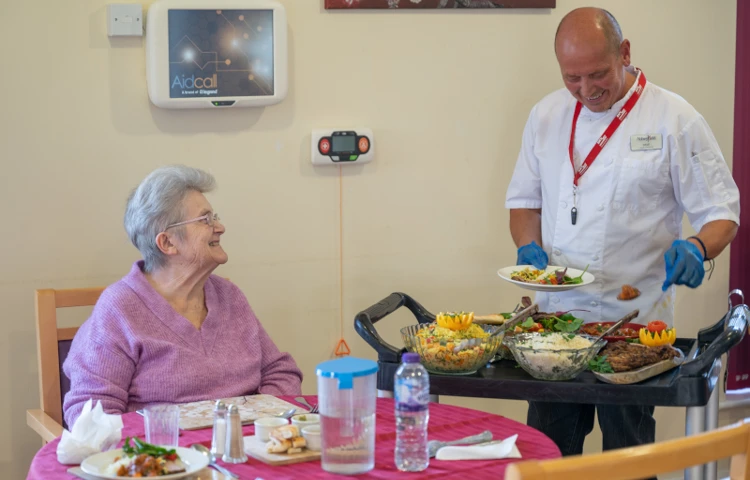 smiling-resident-and-staff-member-serving-up-meal.jpg