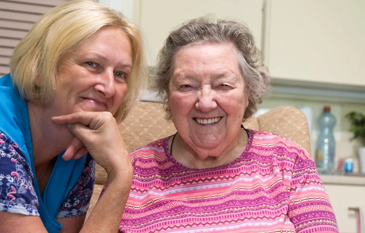 Two women sat smiling for a photo in the kitchen