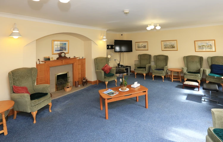 Large lounge area with blue carpet and green chairs at Chirnside House
