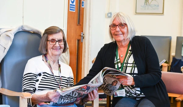 Older Woman And Staff Member Looking Through The Newspaper Together