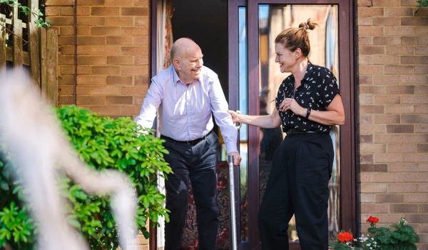 Woman Helping Older Man Outside Into The Sunshine